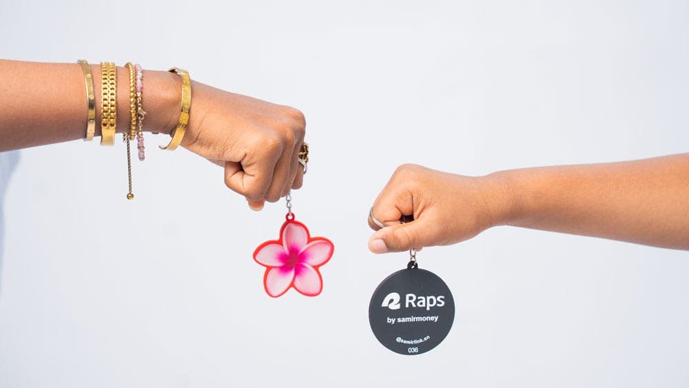 Deux mains tendent chacune un porte-clés : une fleur rose et le porte-clés NFC RAPS by Samir Money